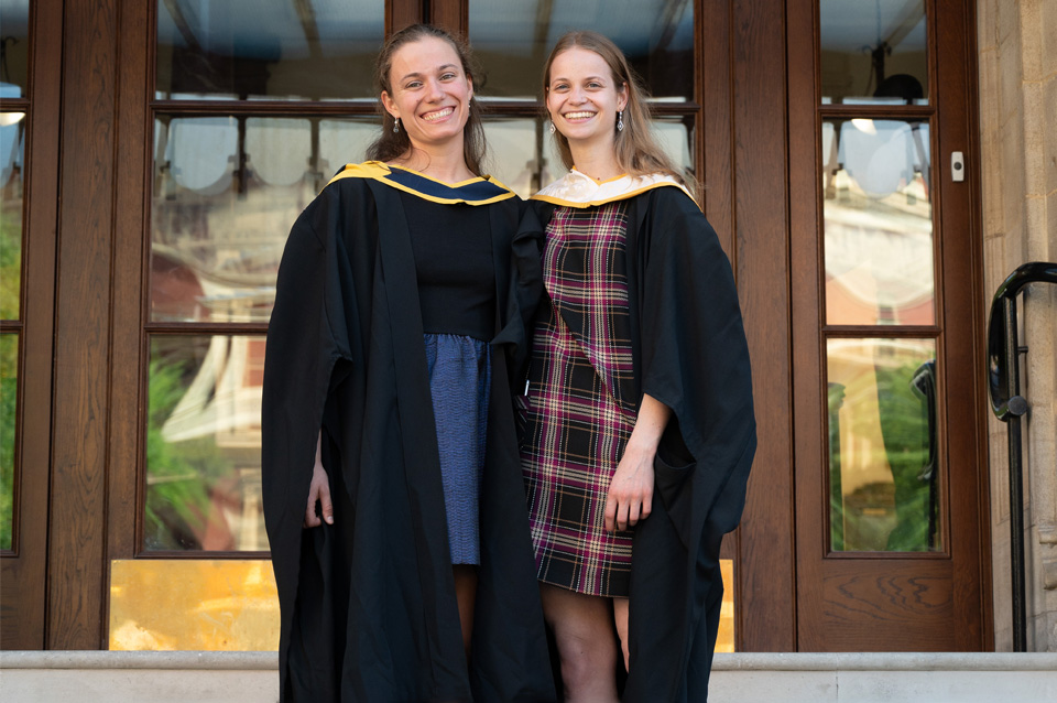 Two female graduates on the steps of the Royal College of Music 